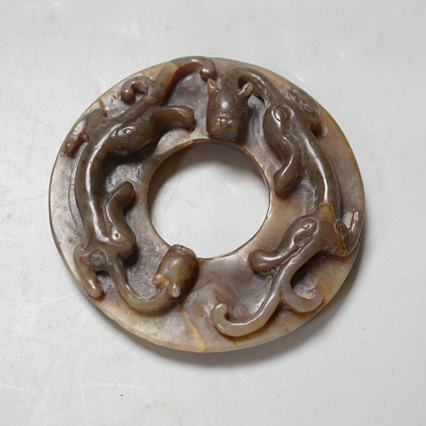 A Chinese brown and celadon jade ‘chilong’ bi disc, probably Ming dynasty, 8cm